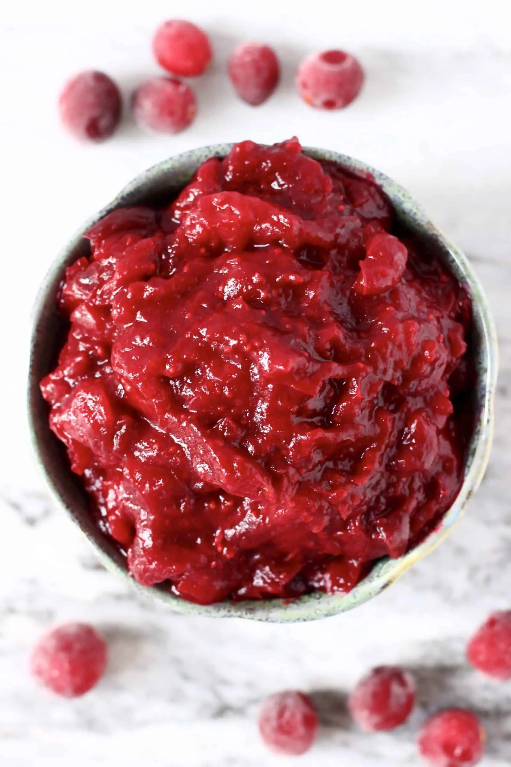 Cranberry sauce in a blue bowl against a marble background with fresh cranberries 