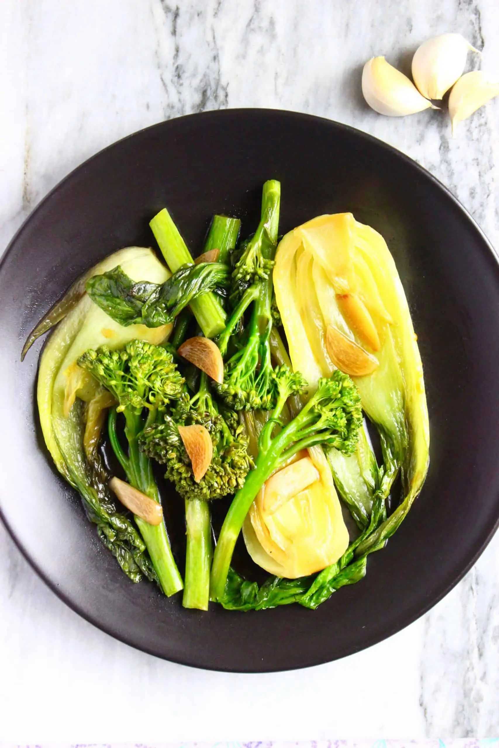 Broccoli, pak choi and sliced garlic in a brown sauce on a black plate