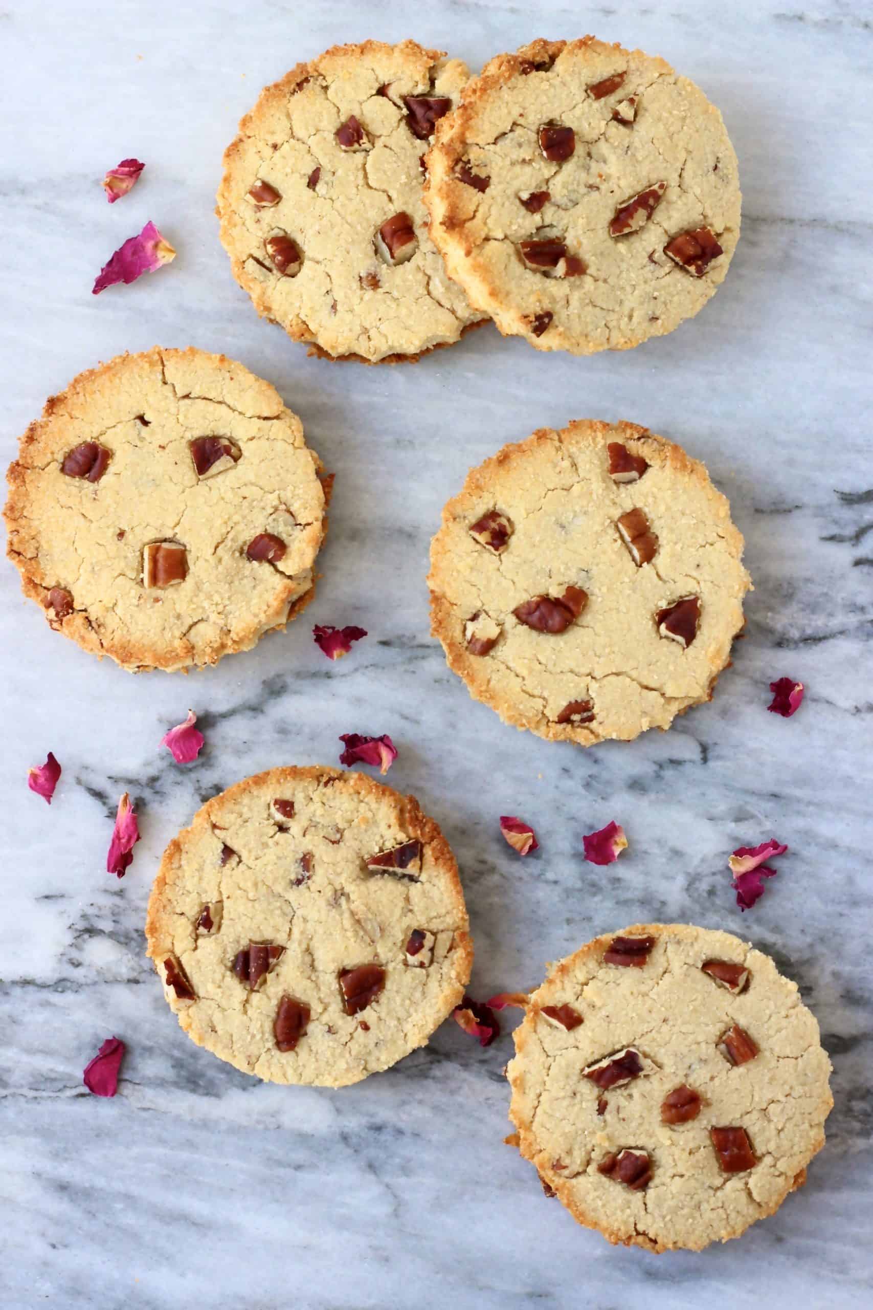 Six round cookies with pecan nuts against a marble background scattered with rose petals