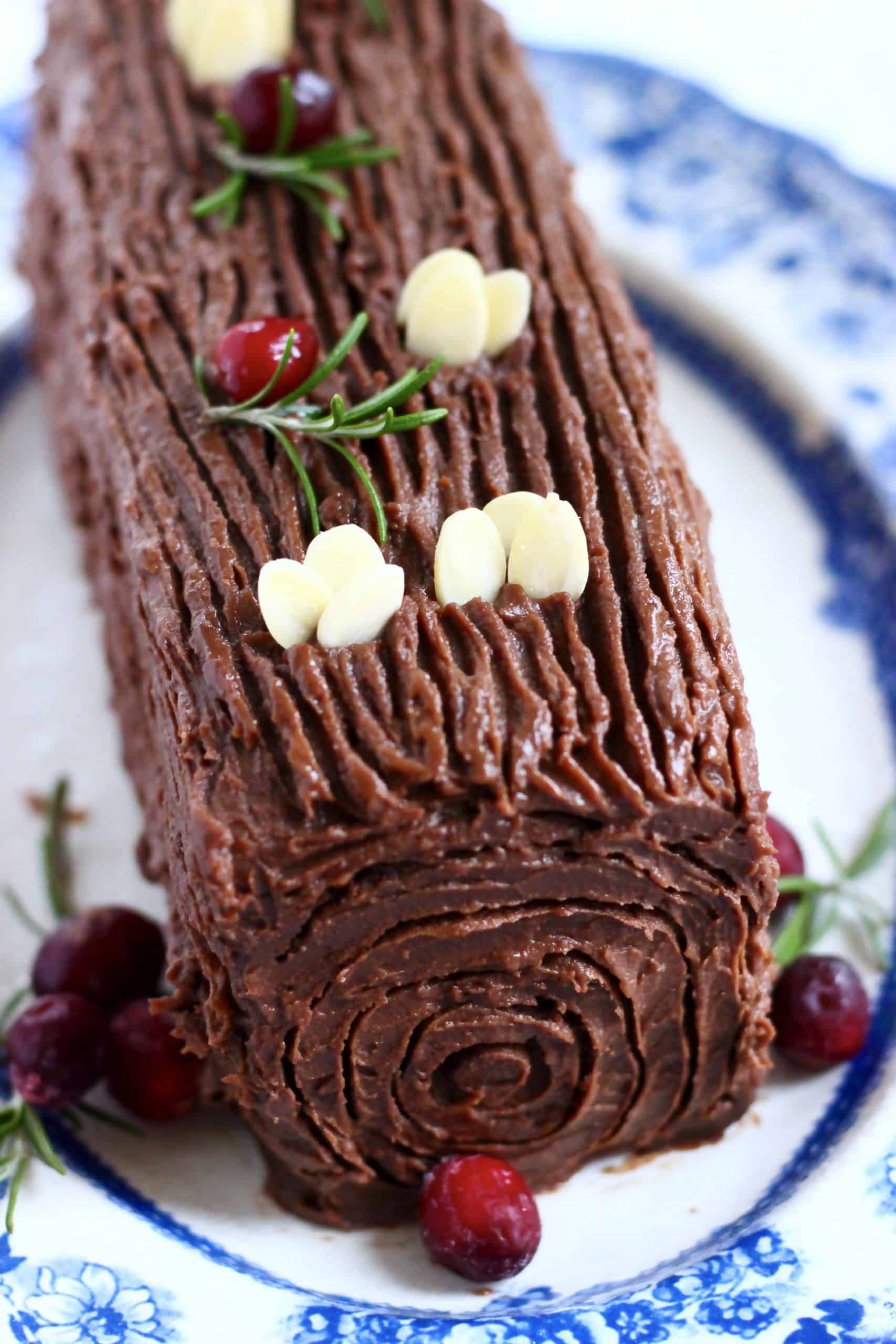 A gluten-free vegan yule log decorated with cranberries, rosemary and flaked almonds