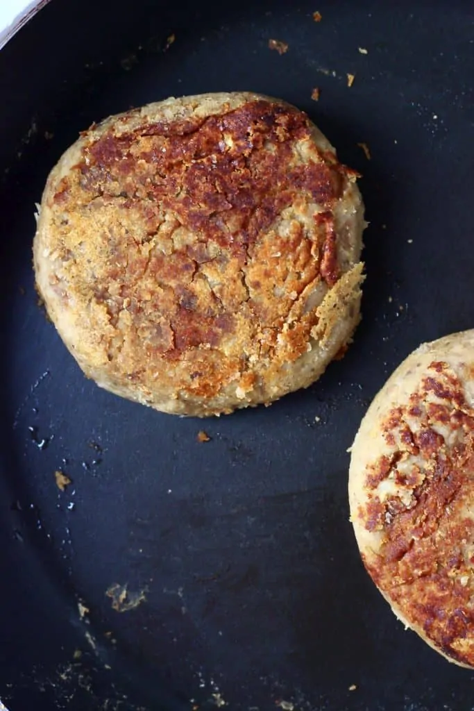 Two golden brown vegan Christmas burger patties in a black frying pan