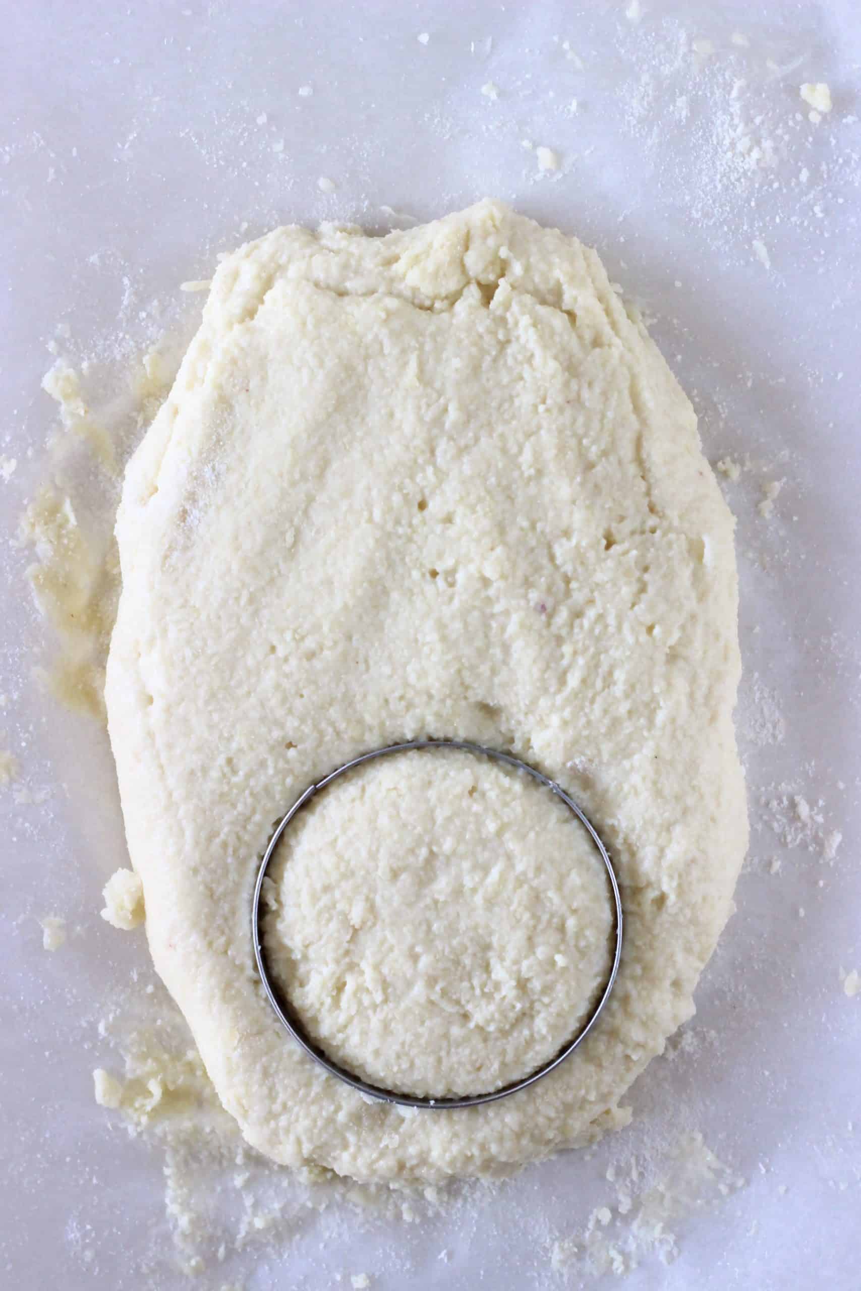 Gluten-free vegan biscuits dough on baking paper with a circular cookie cutter cutting out a circle
