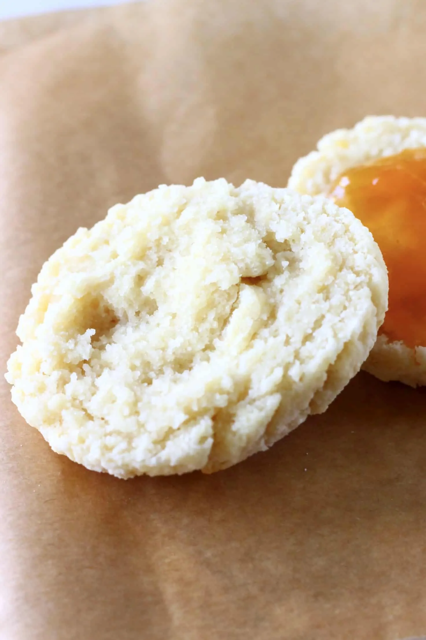 A halved gluten-free vegan biscuit with one half spread with apricot jam