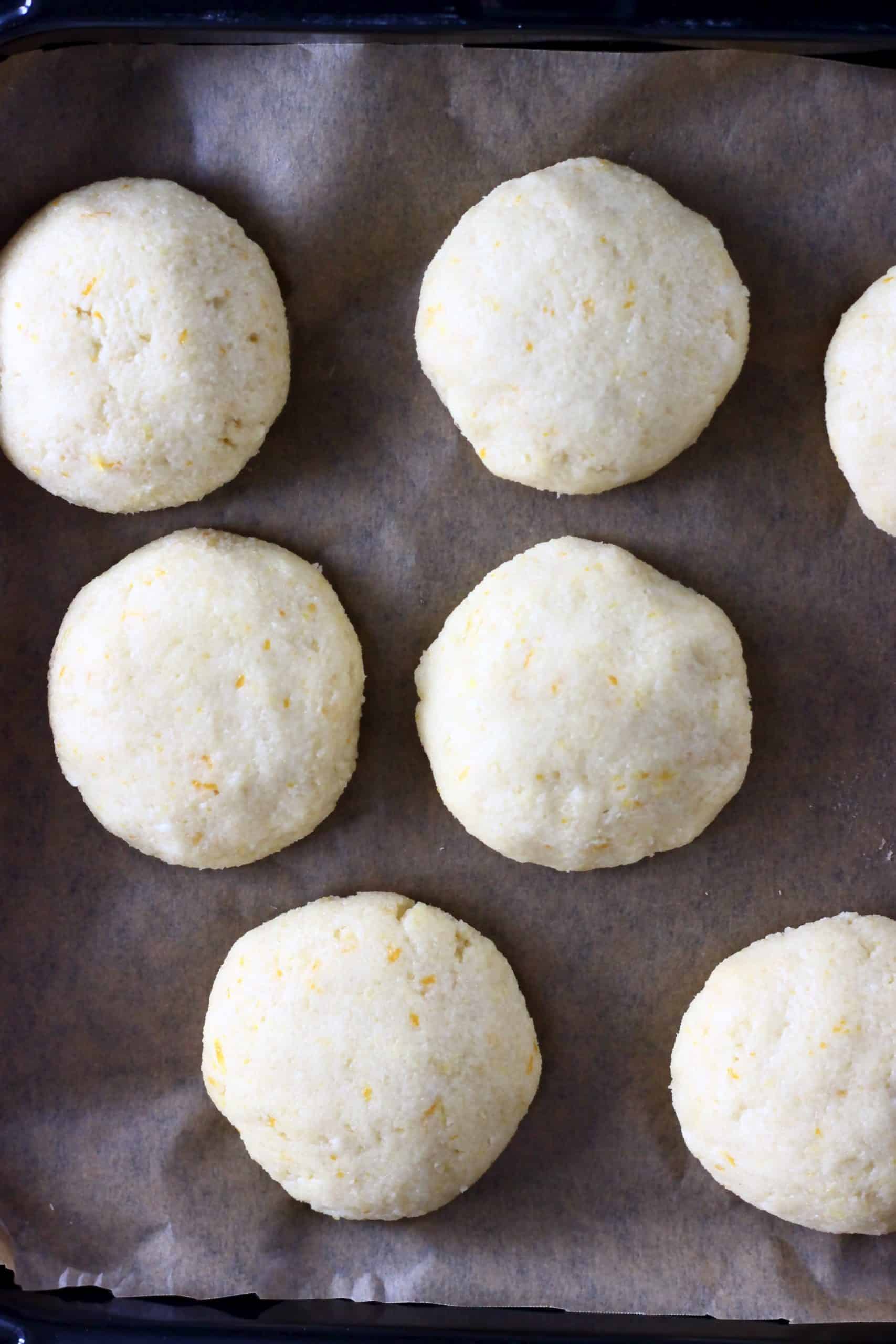Seven raw gluten-free vegan orange cookies on a baking tray lined with baking paper