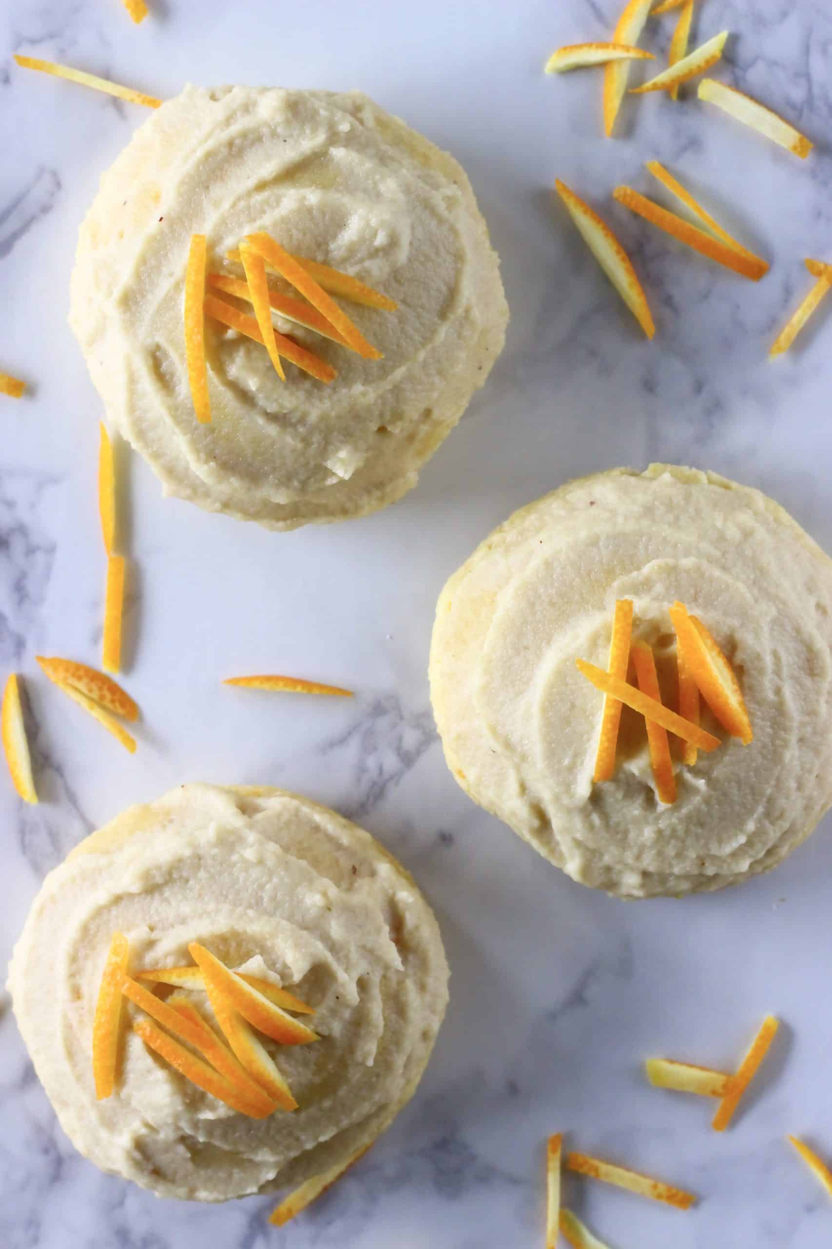 Three gluten-free vegan orange cookies with frosting and orange zest
