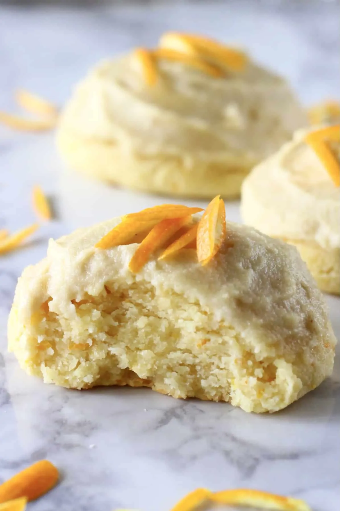 Three orange cookies with frosting and orange zest with a bite taken out of one
