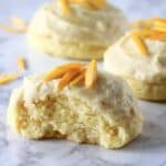 Three gluten-free vegan orange cookies with frosting and orange zest with a bite taken out of one