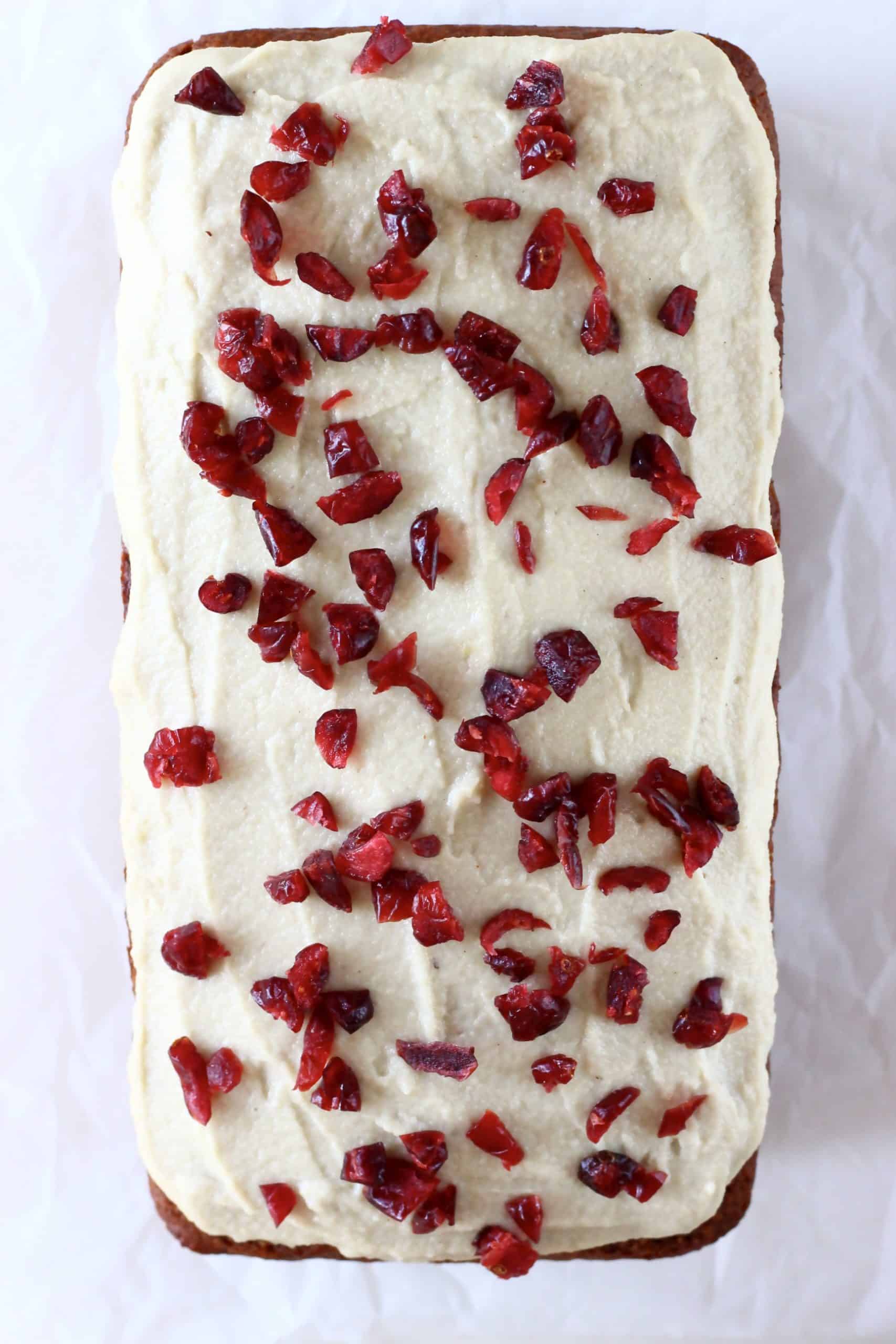 A gluten-free vegan gingerbread loaf cake with vegan cream cheese frosting and dried cranberries on top
