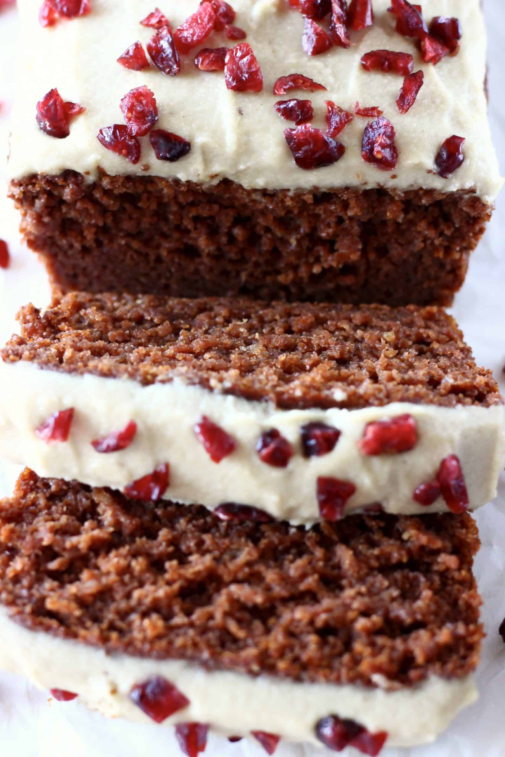 A gluten-free vegan gingerbread loaf cake topped with white frosting and dried cranberries with two slices next to it