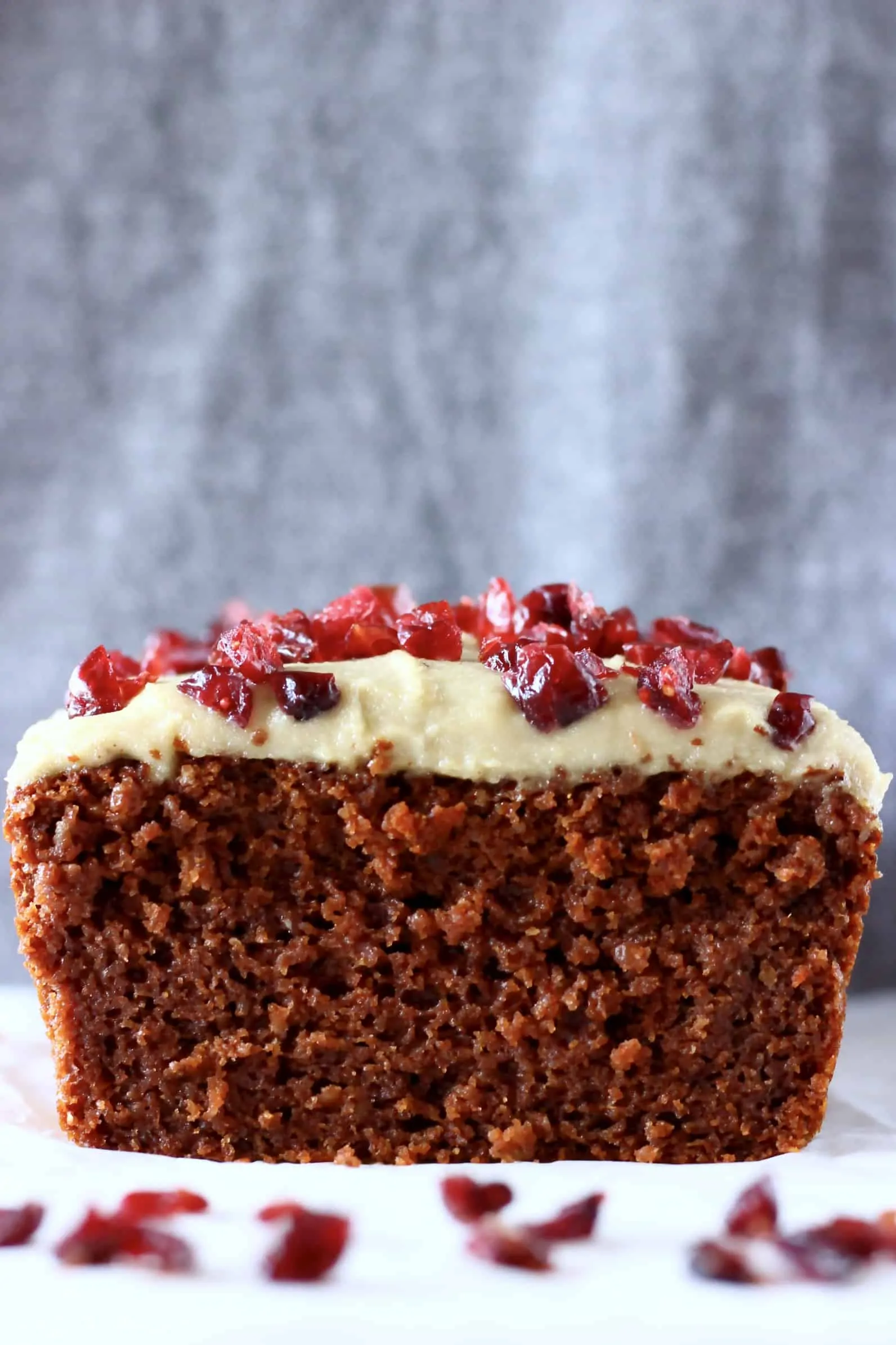Sliced gluten-free vegan gingerbread loaf cake topped with white frosting and dried cranberries