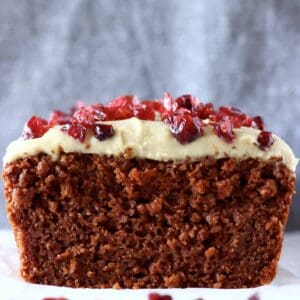 Sliced gluten-free vegan gingerbread loaf cake topped with white frosting and dried cranberries