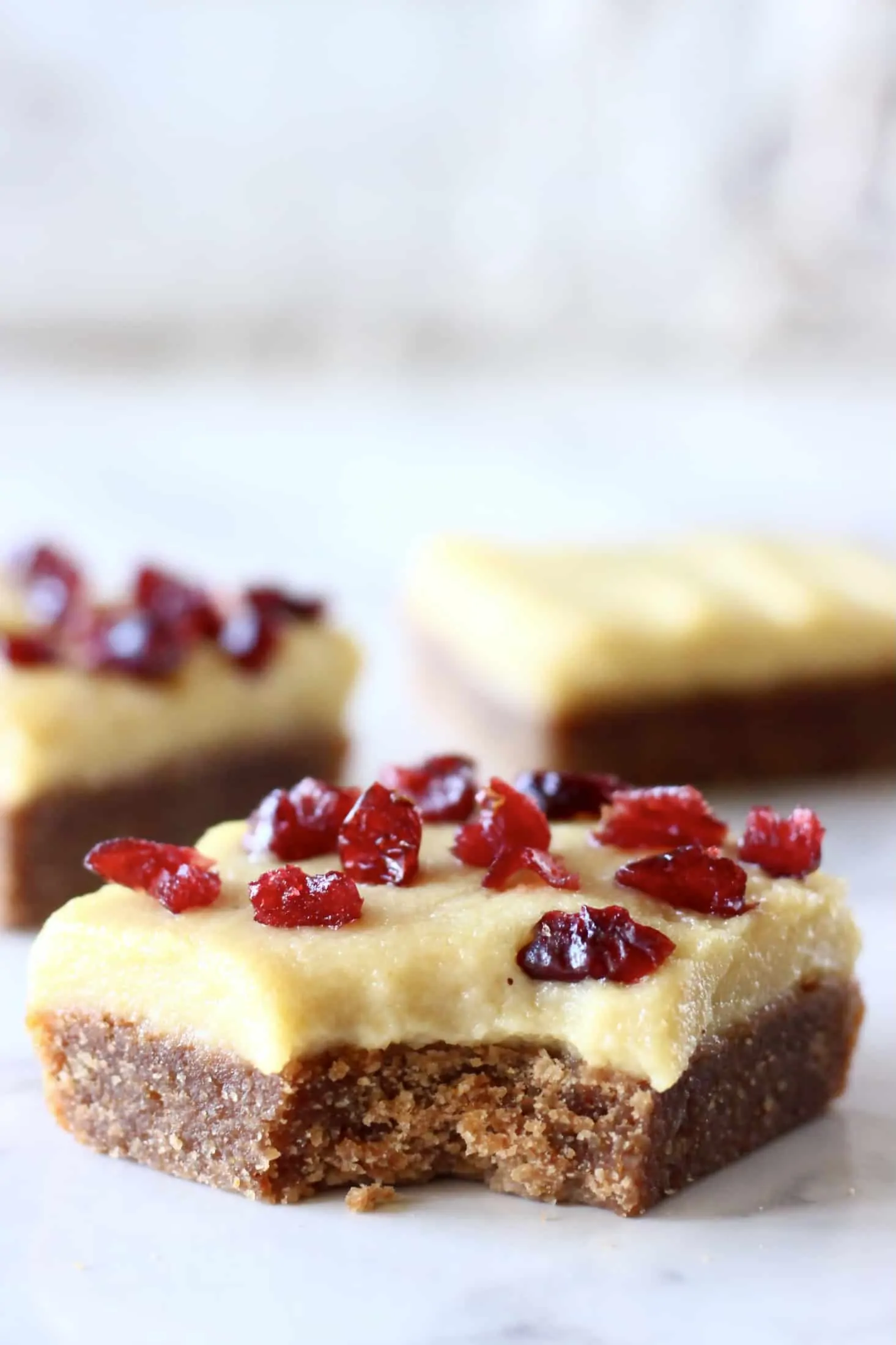 Three gingerbread cookie bars with frosting and dried cranberries with a bite taken out of one