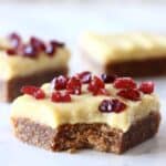 Three gluten-free vegan gingerbread cookie bars with frosting and dried cranberries with a bite taken out of one