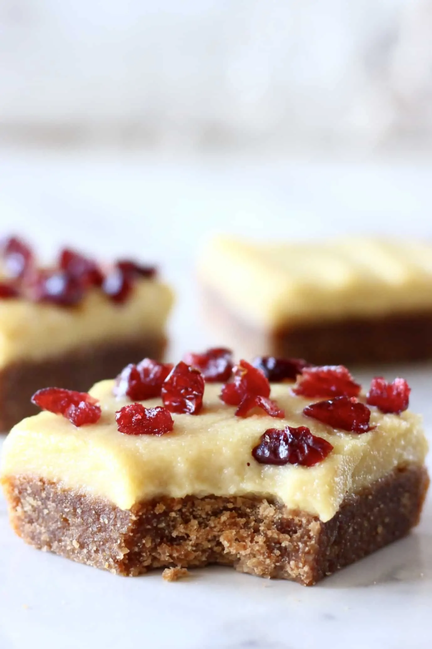 Three gluten-free vegan gingerbread cookie bars with frosting and dried cranberries with a bite taken out of one