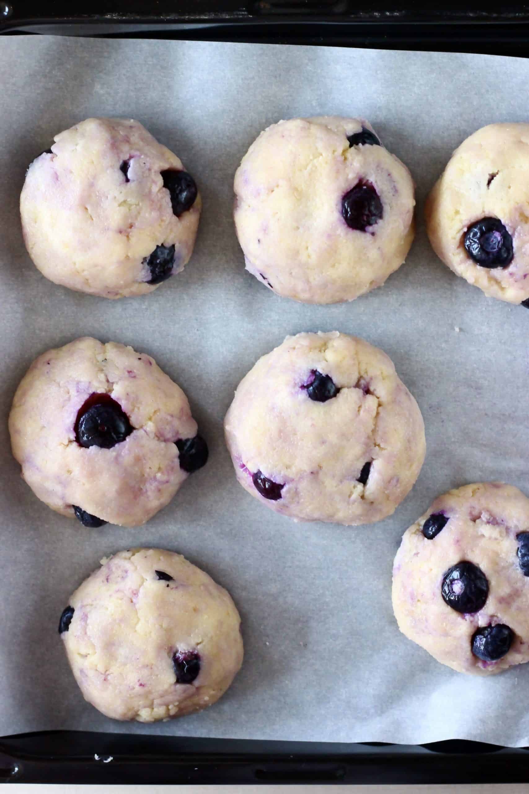 Seven raw gluten-free vegan lemon blueberry cookies on a baking tray lined with baking paper