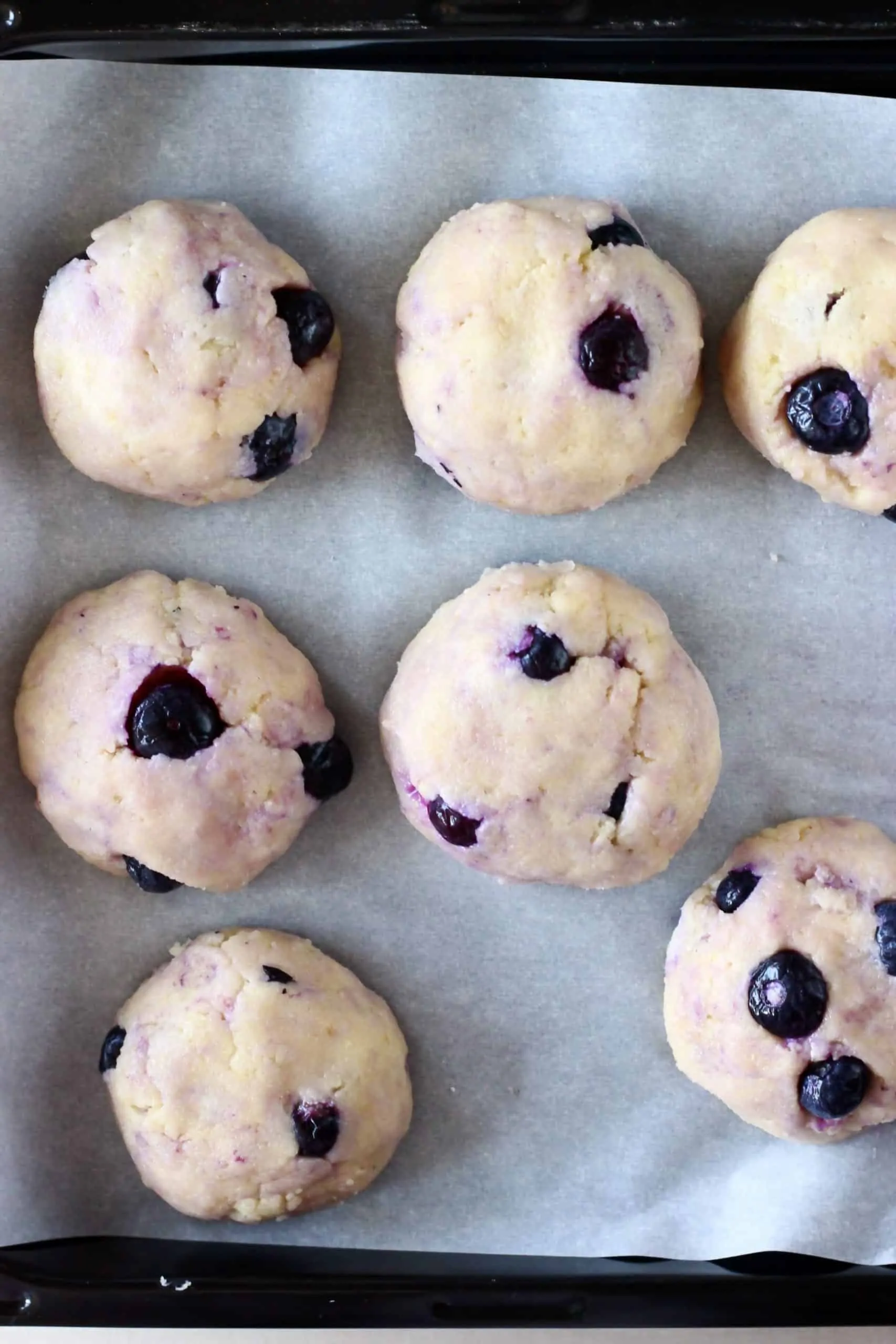 Seven raw gluten-free vegan lemon blueberry cookies on a baking tray lined with baking paper