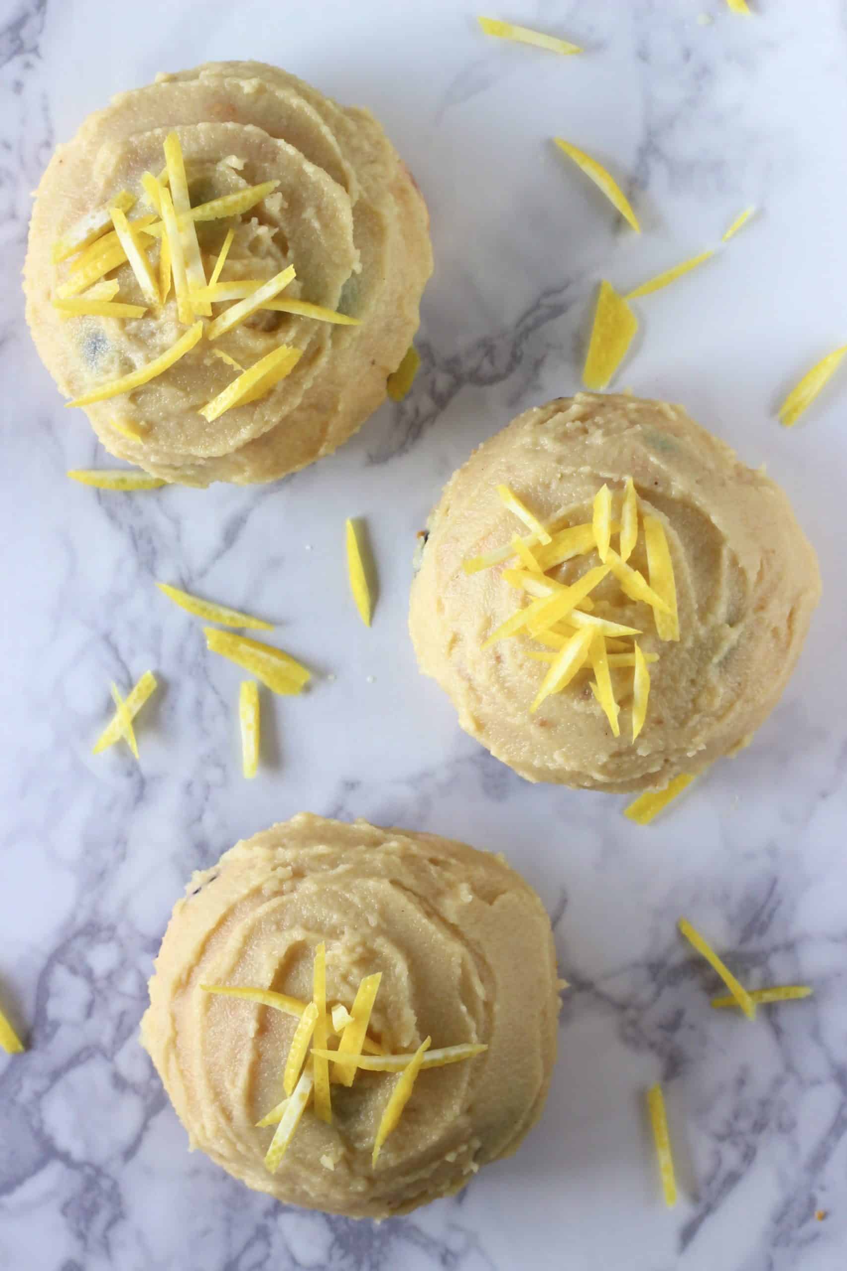 Three gluten-free vegan lemon blueberry cookies covered with lemon frosting and lemon zest