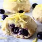 Three gluten-free vegan lemon blueberry cookies with frosting and a bite taken out of one