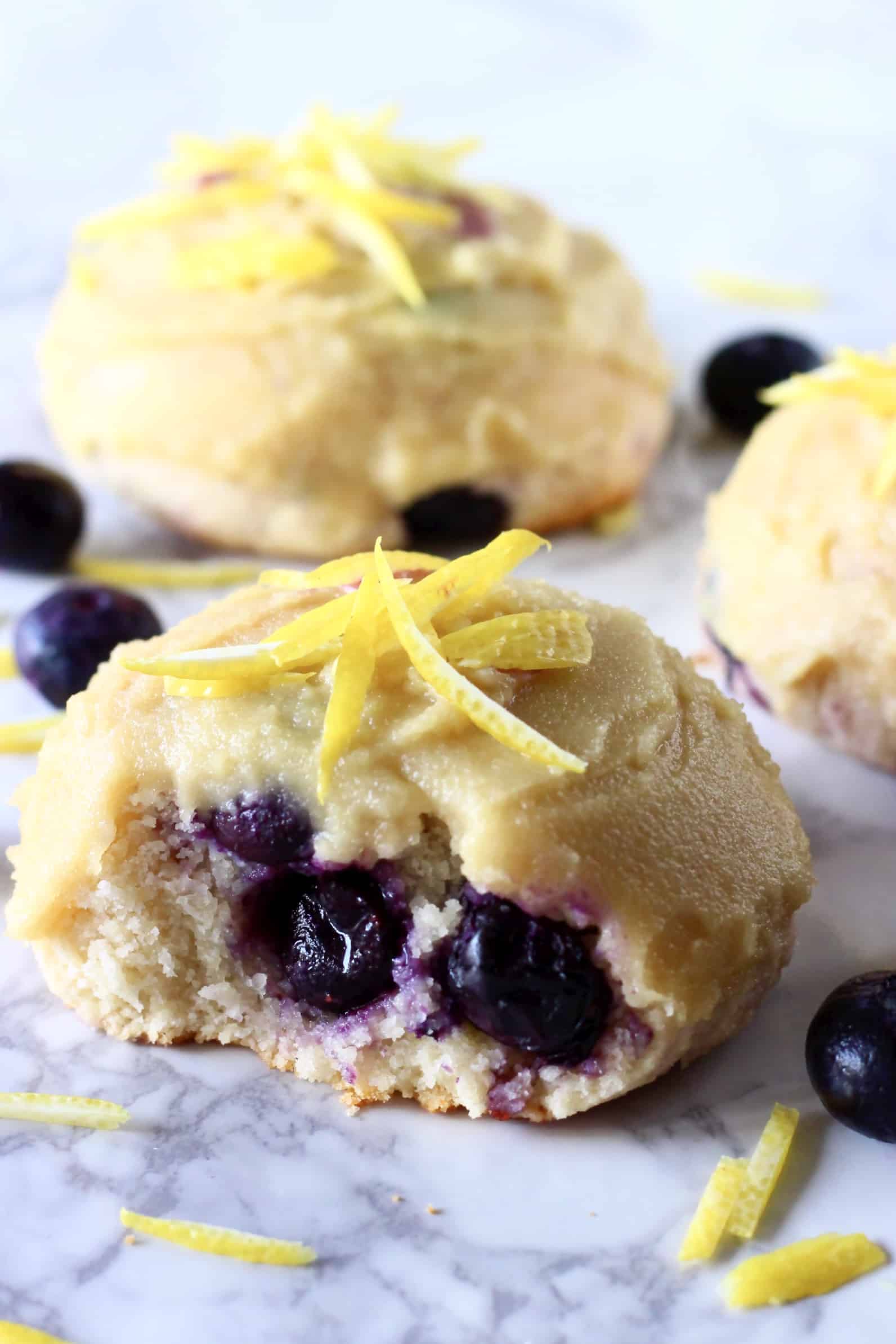 Three gluten-free vegan lemon blueberry cookies with frosting and a bite taken out of one