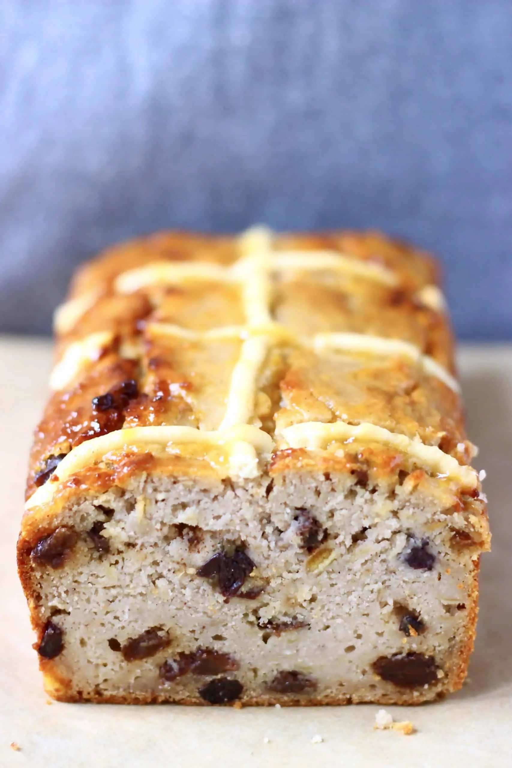 Hot cross bun loaf on a sheet of brown baking paper against a grey background