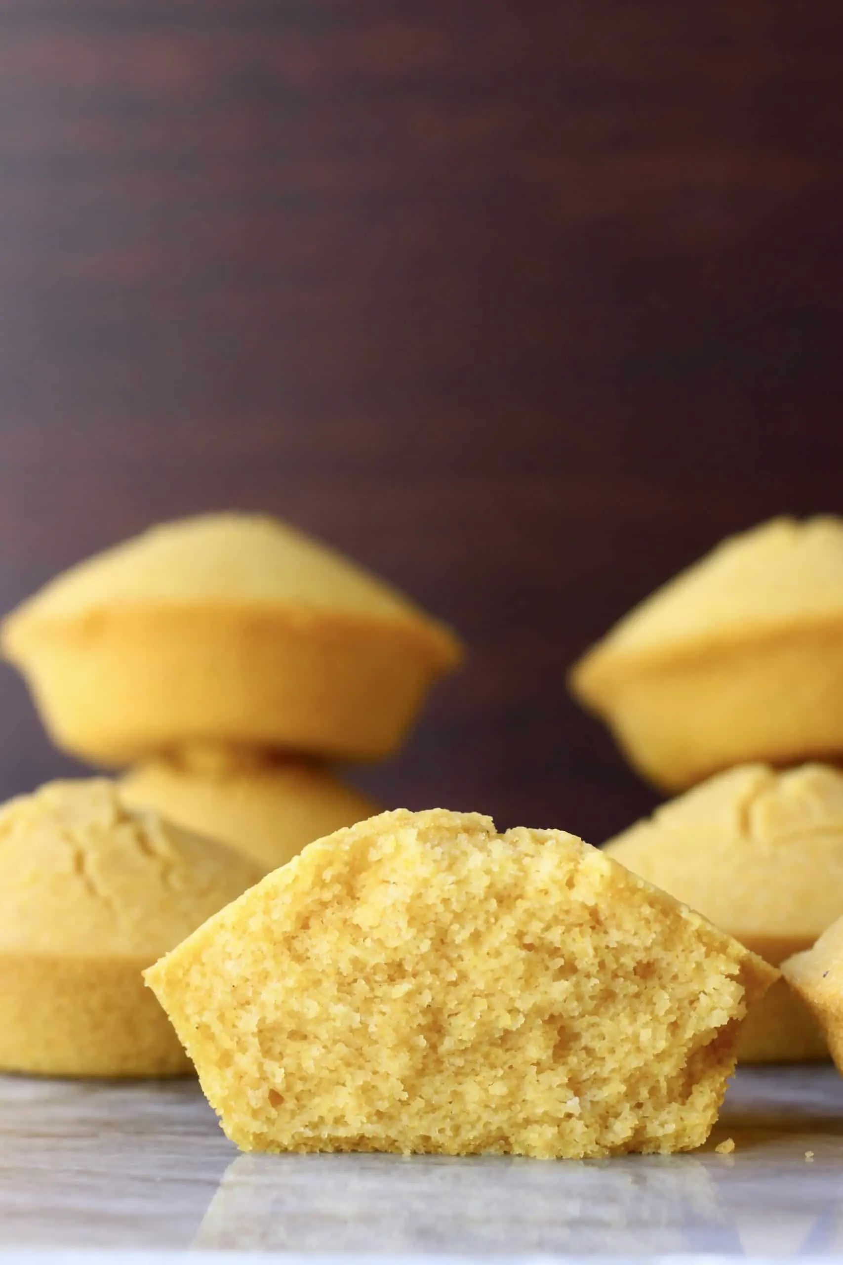 Six cornbread muffins with one cut in half on a marble slab against a dark brown background
