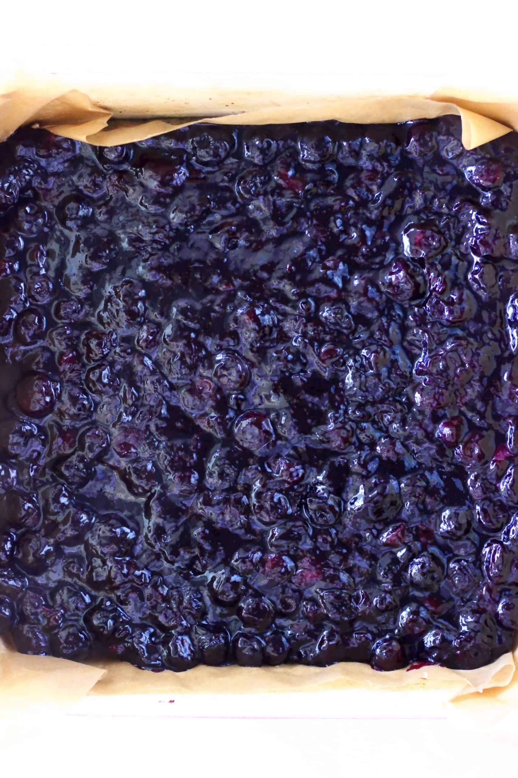 Cooked blueberry mixture on top of baked crumble base in a square baking tin