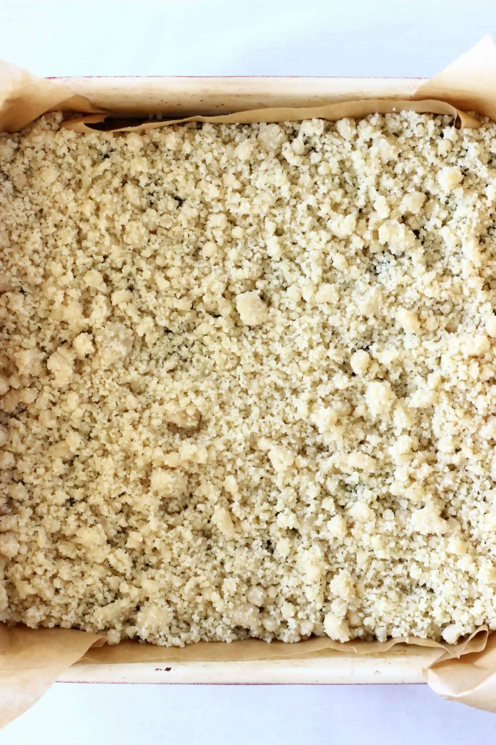 Raw crumble dough on top of blueberry mixture in a square baking tin