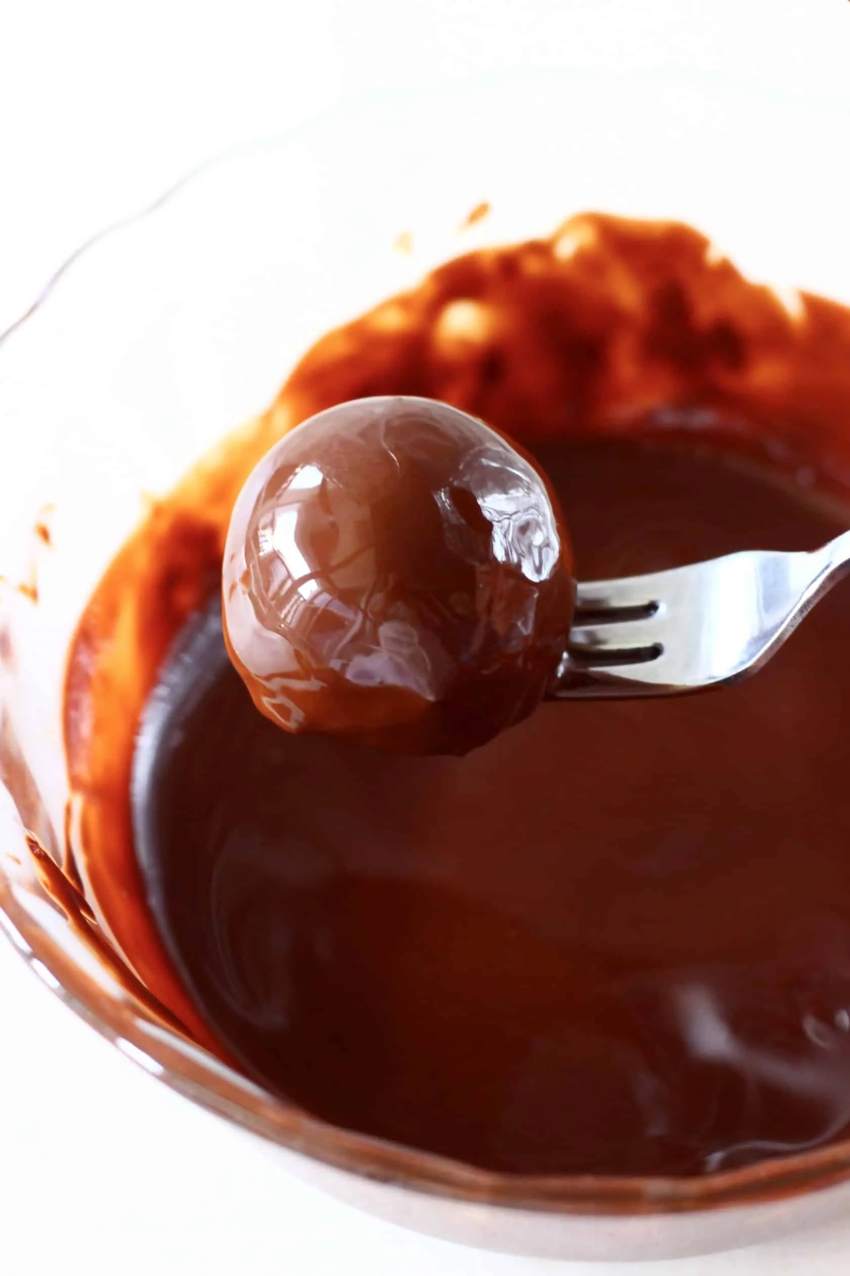 A healthy peanut butter ball being lifted out of a bowl of melted chocolate with a fork
