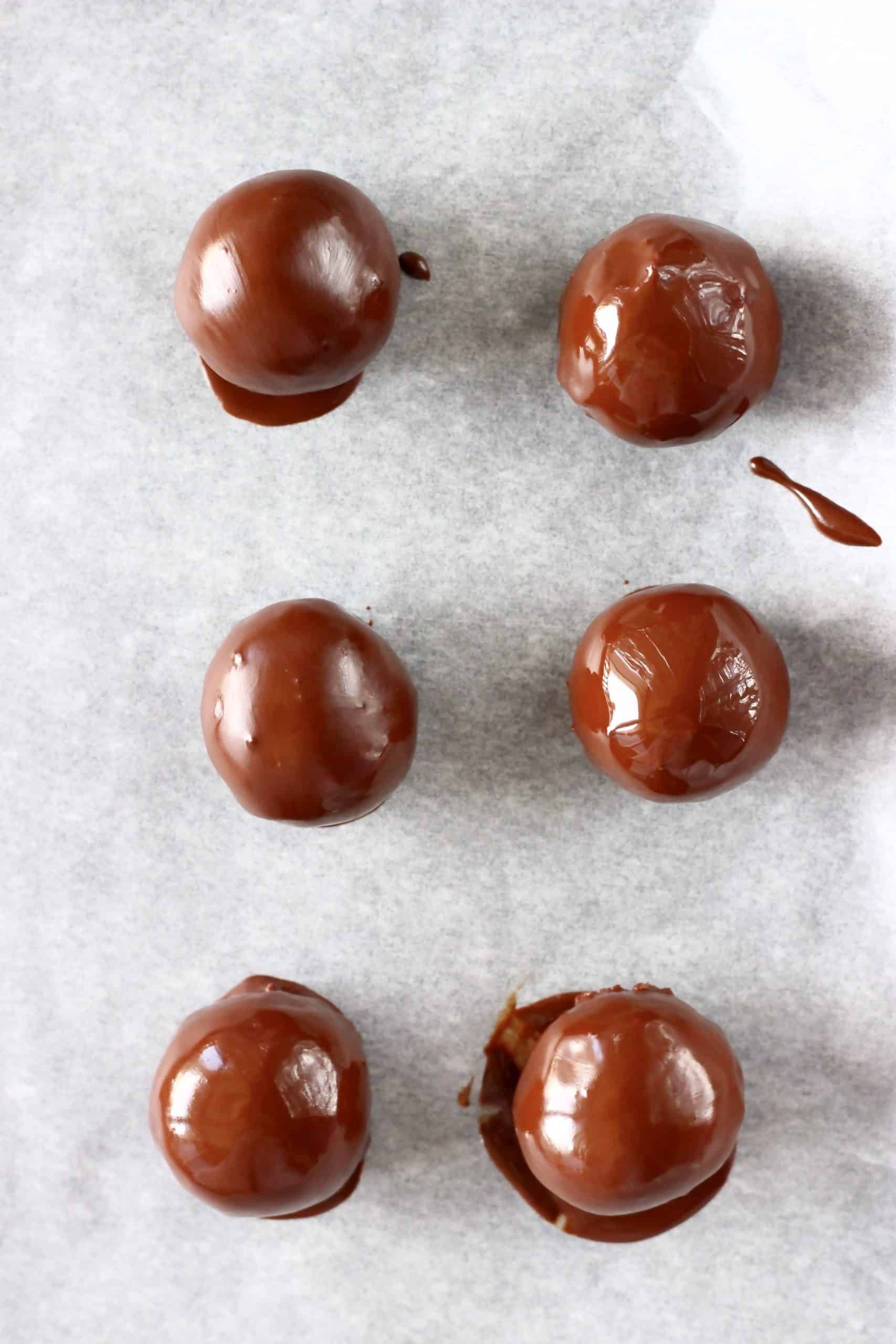 Six healthy peanut butter balls dipped with melted chocolate on a baking tray lined with baking paper