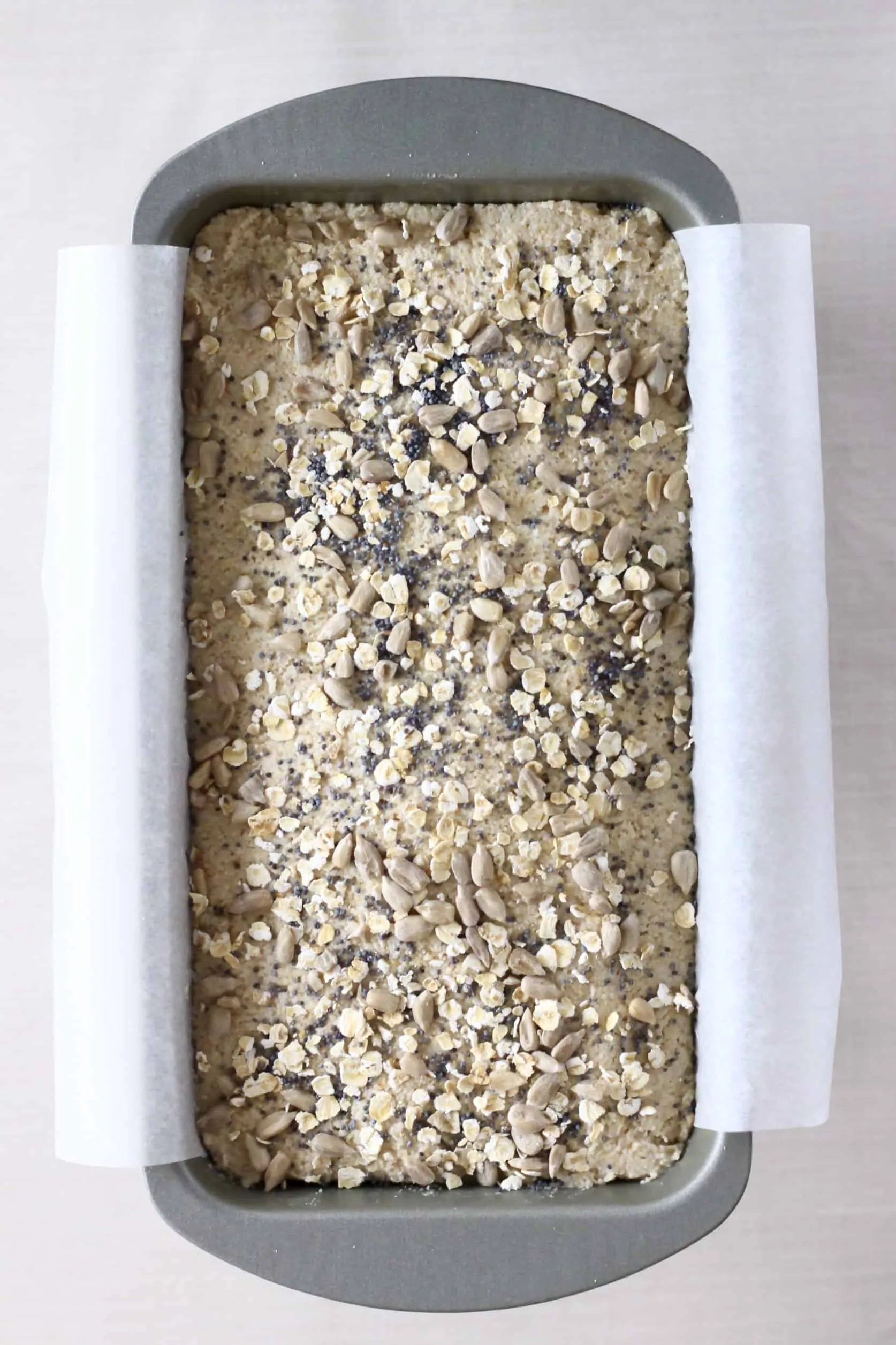 Oat flour bread dough topped with oats and seeds in a loaf tin