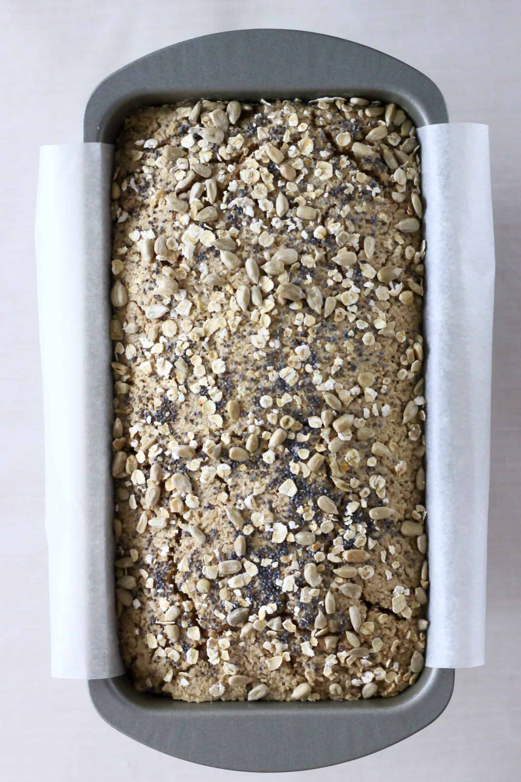 Oat flour bread topped with oats and seeds in a loaf tin