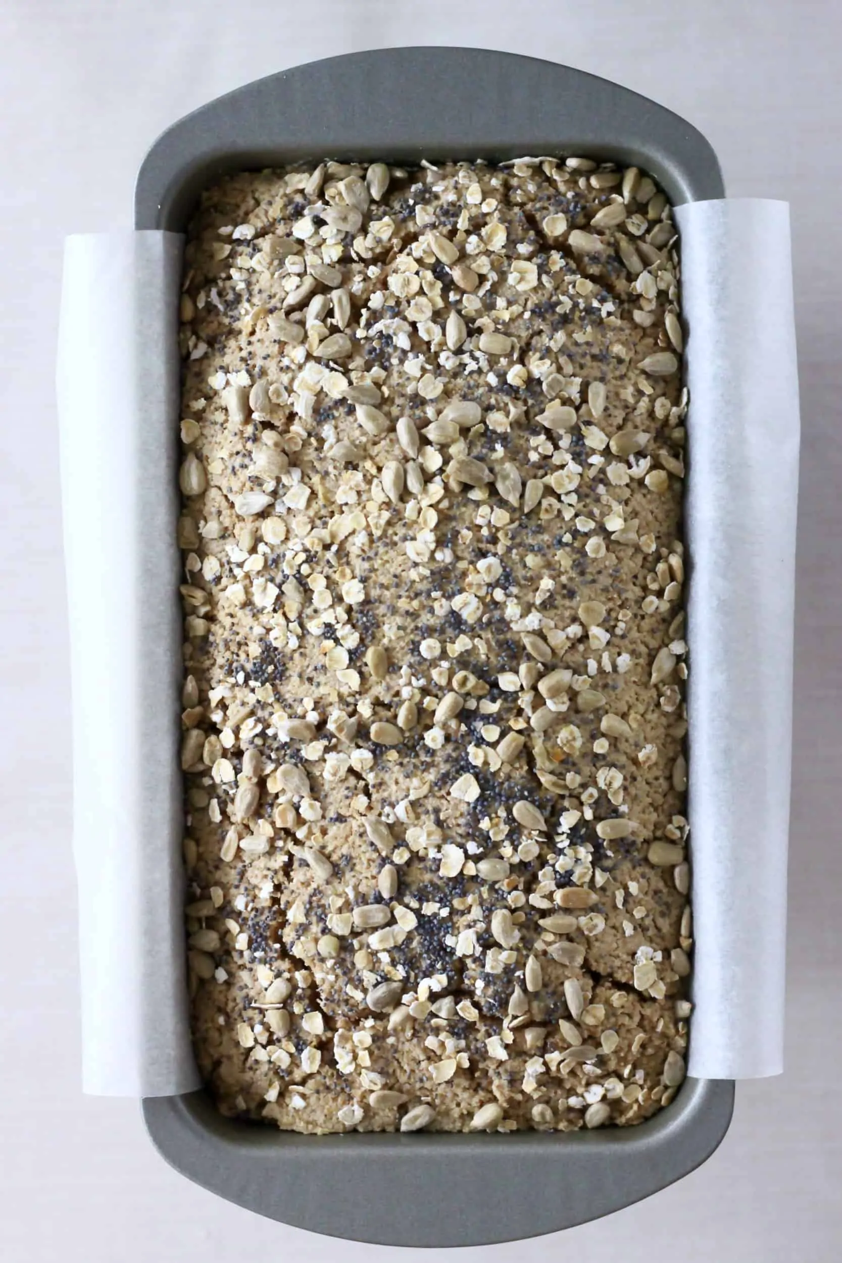 Oat flour bread topped with oats and seeds in a loaf tin