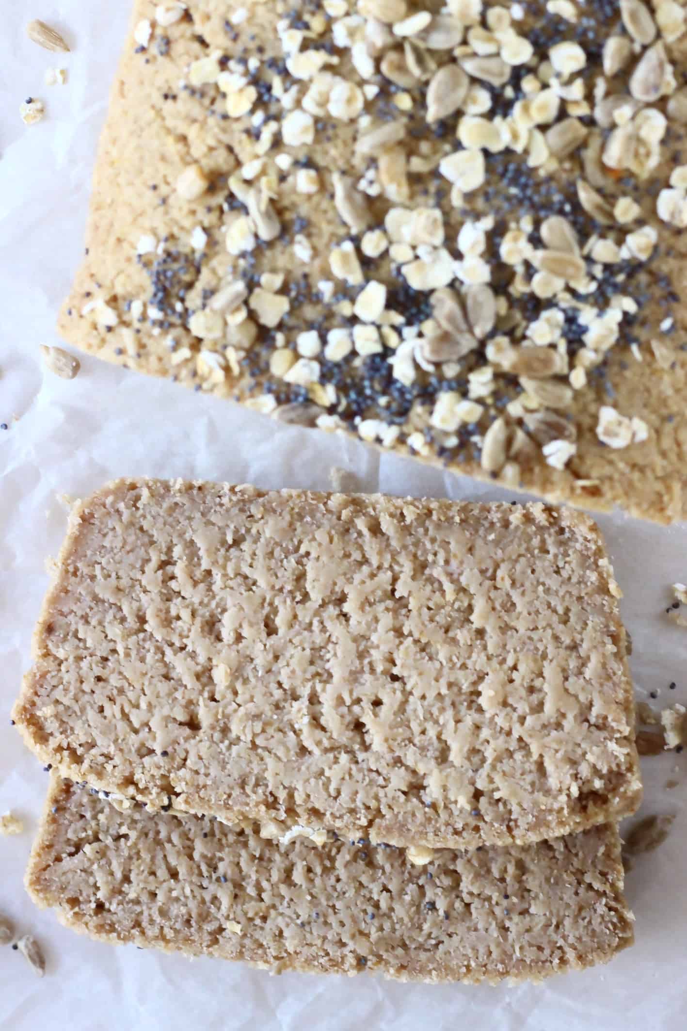 A loaf of oat flour bread topped with oats and seeds with two slices next to it