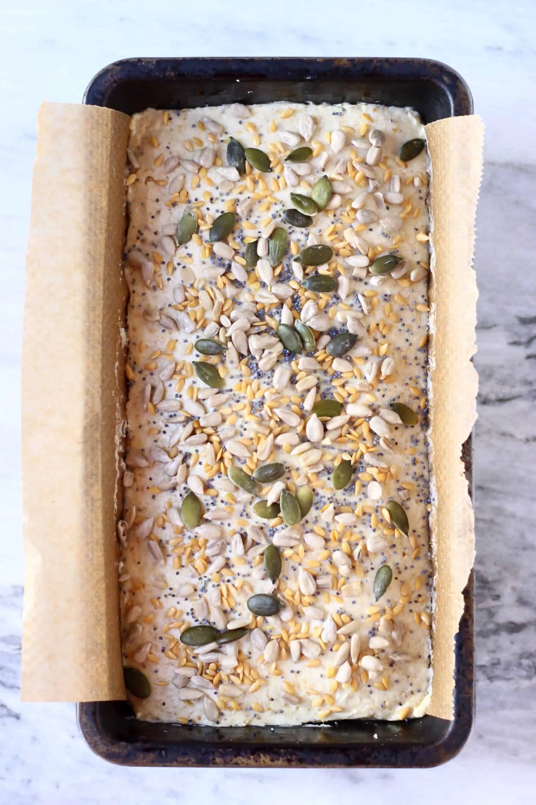 Flaxseed bread dough topped with mixed seeds in a loaf tin lined with baking paper