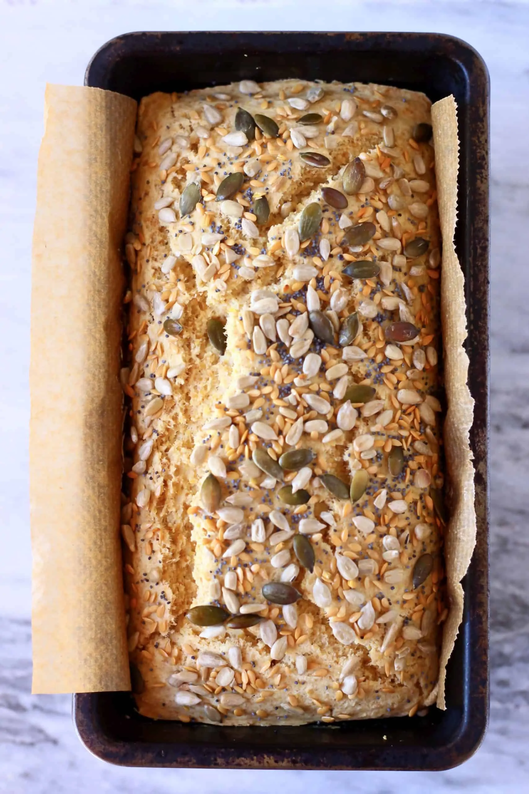 A loaf of flaxseed bread topped with seeds in a loaf tin