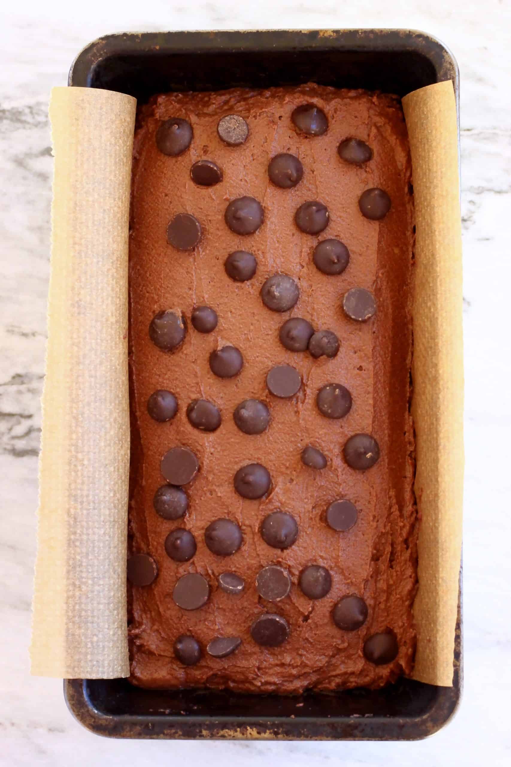 Raw sweet potato chocolate cake batter topped with chocolate chips in a loaf tin lined with baking paper