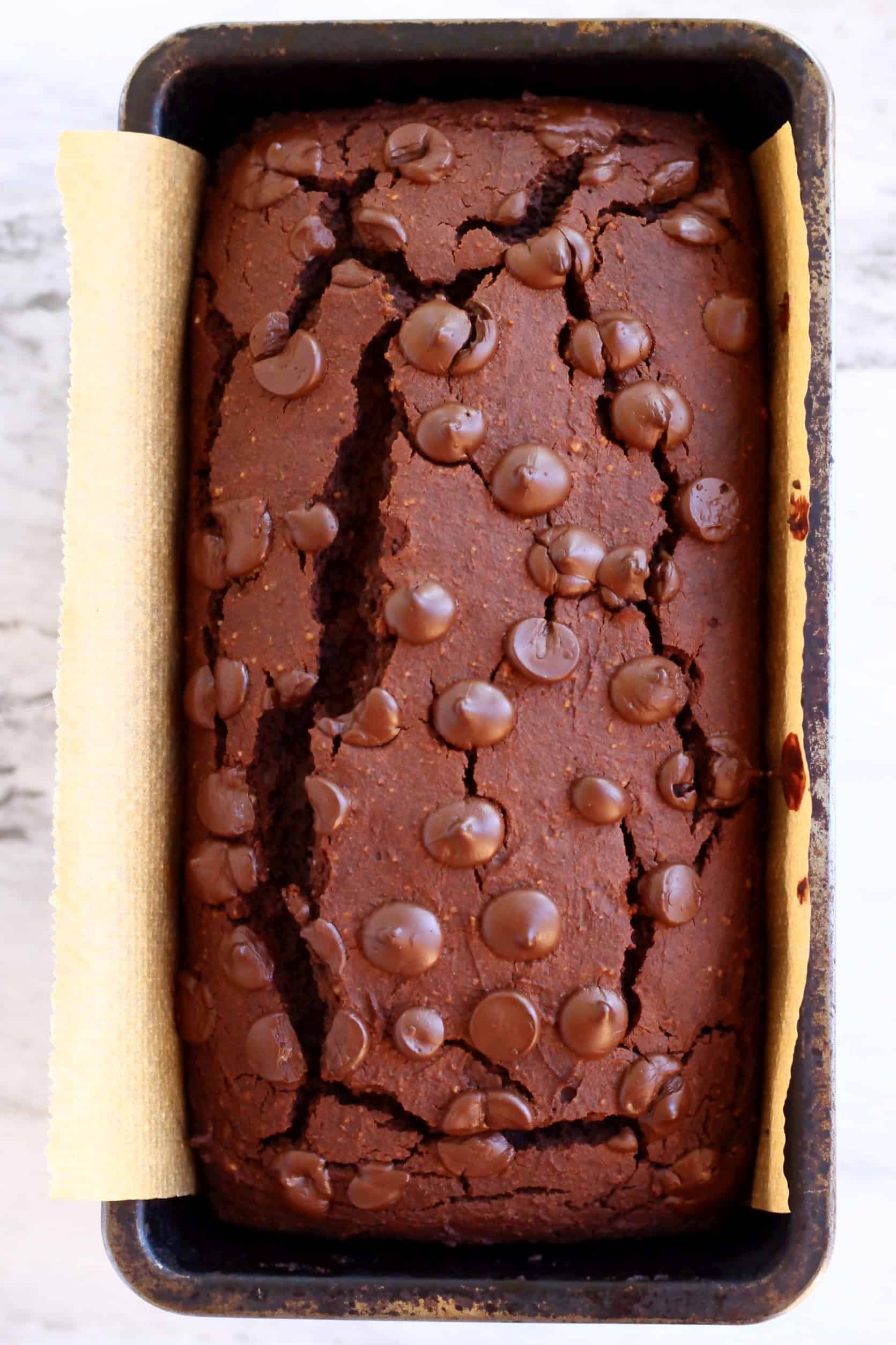 Sweet potato chocolate cake loaf topped with chocolate chips in a loaf tin lined with baking paper