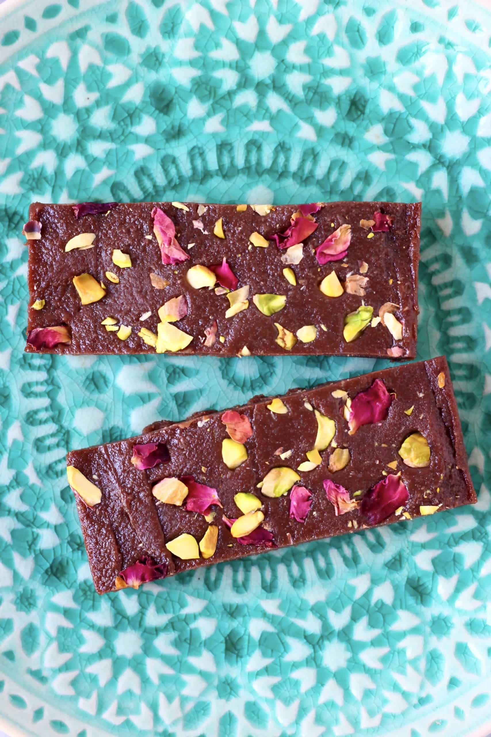 Two rectangular chocolate bars topped with chopped pistachios and rose petals 