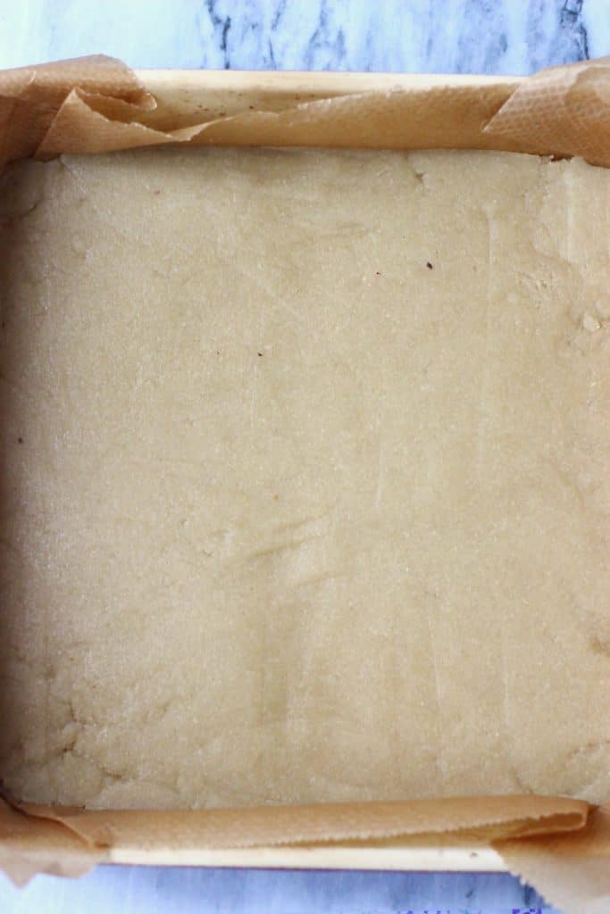 Raw crumble bar dough along the bottom of a square baking tin