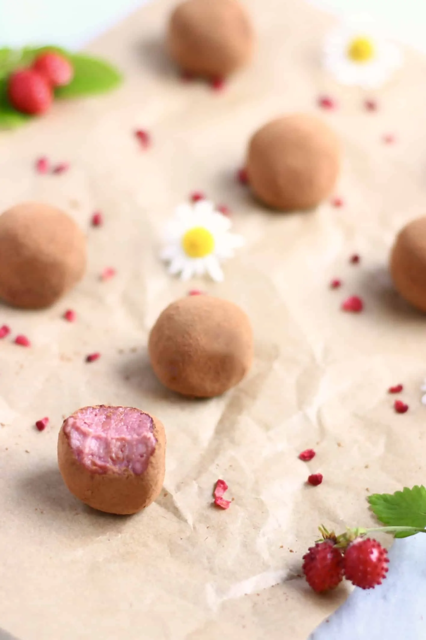 Six strawberry truffles covered in cocoa powder with a mouthful taken out of one