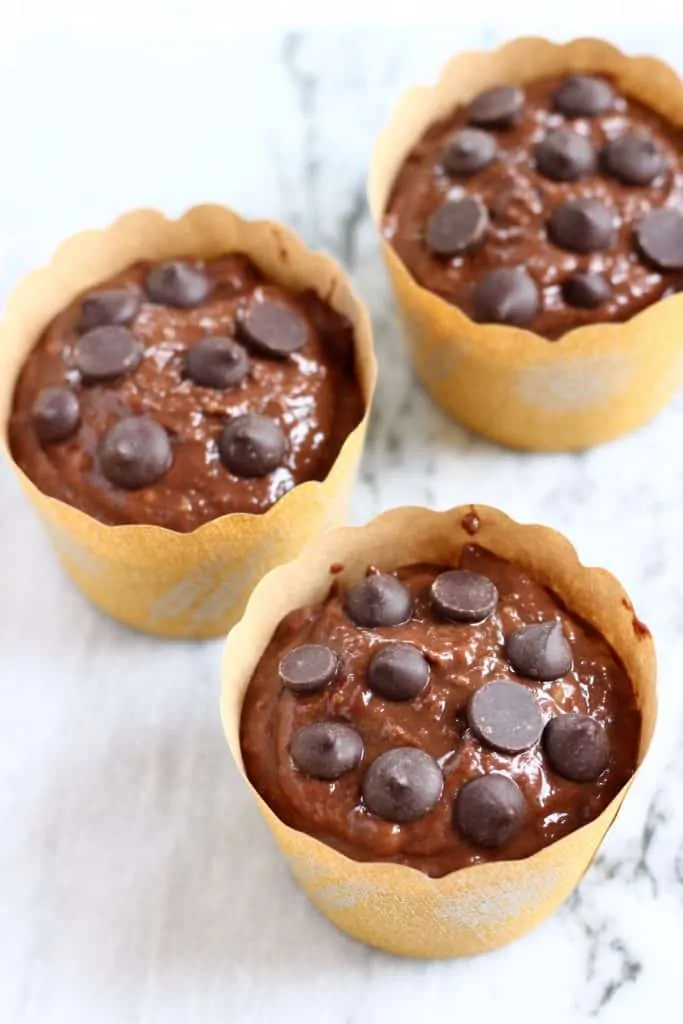 Chocolate muffin batter in three muffin cases topped with chocolate chips