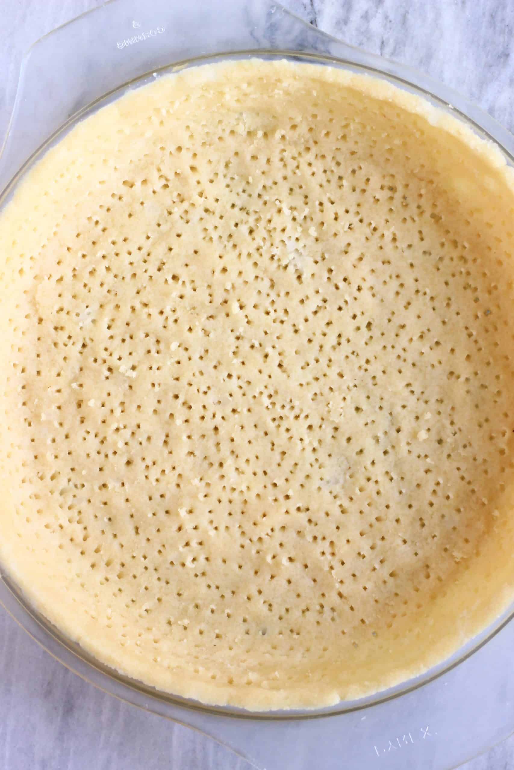 Raw gluten-free vegan pastry dough in a pie dish making a pie crust with fork holes in it