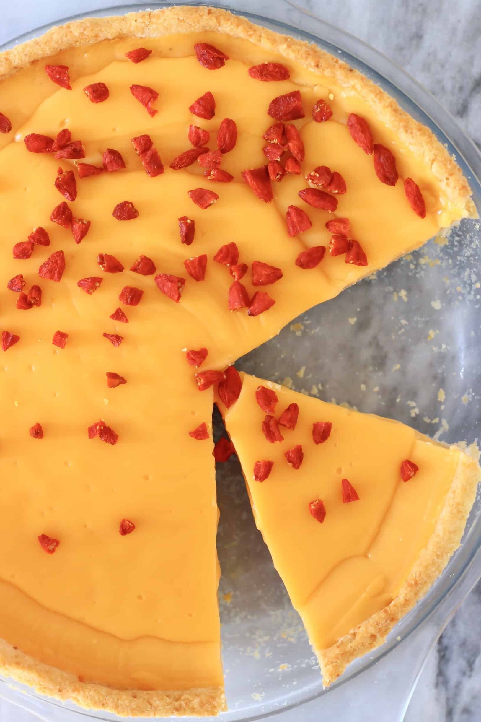 Gluten-free vegan lemon tart topped with goji berries with a slice taken out of it