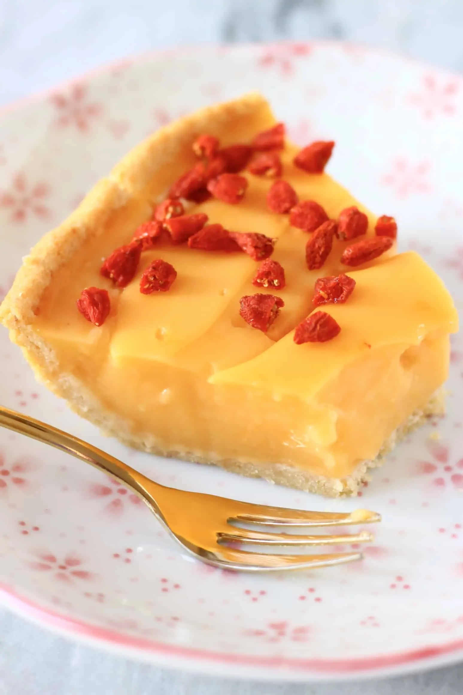 A slice of gluten-free vegan lemon tart on a plate with a gold fork