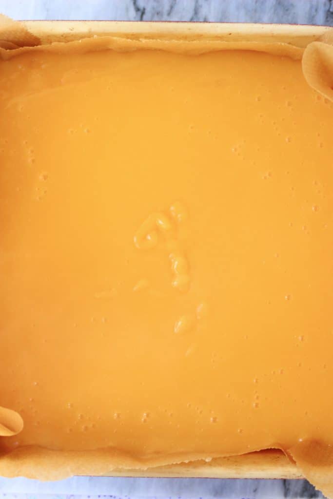 Lemon curd on top of crumble bar base in a square baking tin