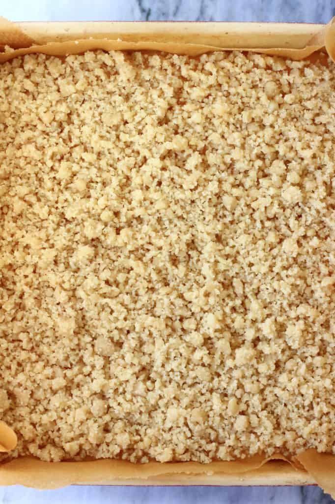 Crumble bar dough sprinkled over lemon curd in a square baking tin