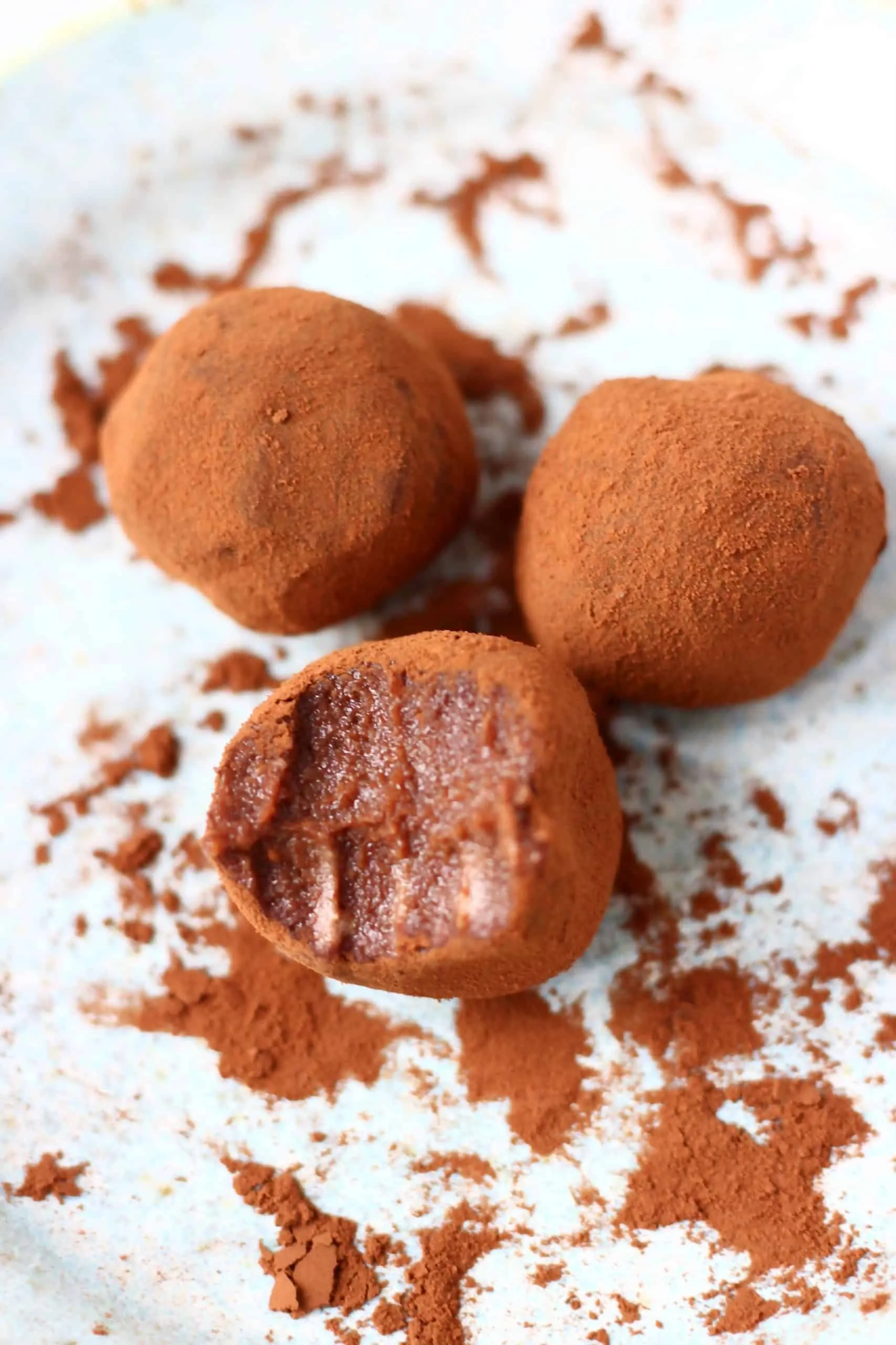 Three chocolate truffles dusted with cocoa powder with a bite taken out of one