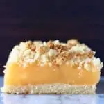 A lemon crumble bar on a marble slab against a brown background