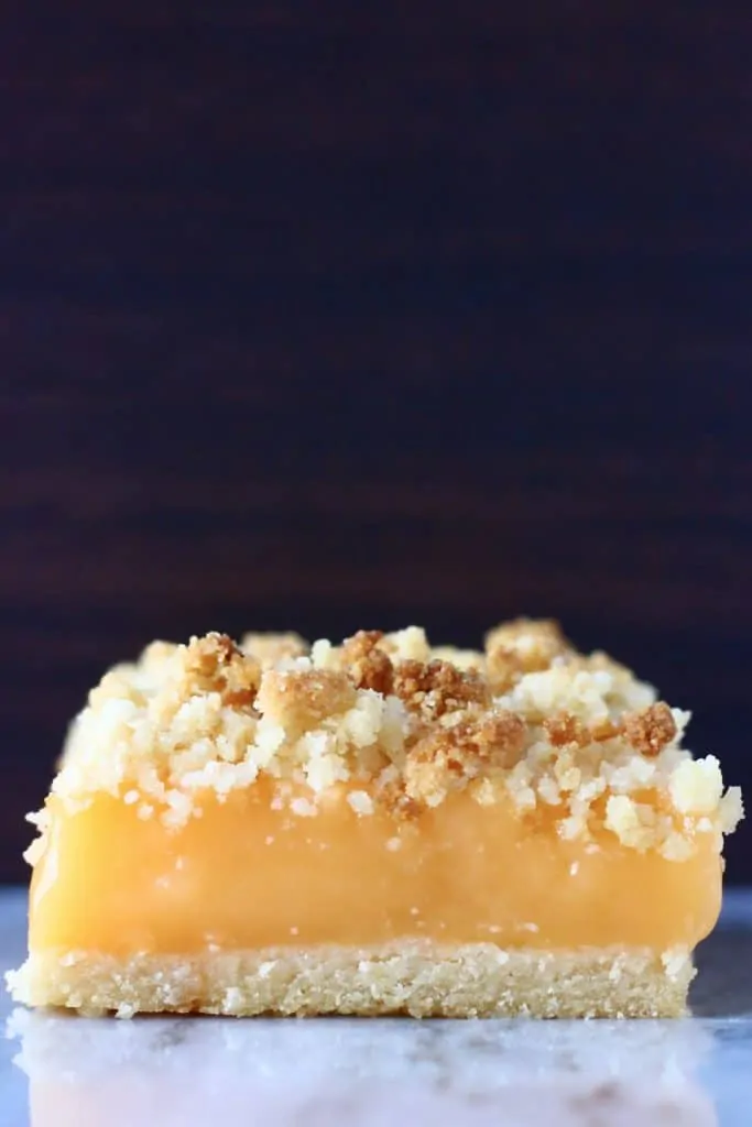 A lemon crumble bar on a marble slab against a brown background