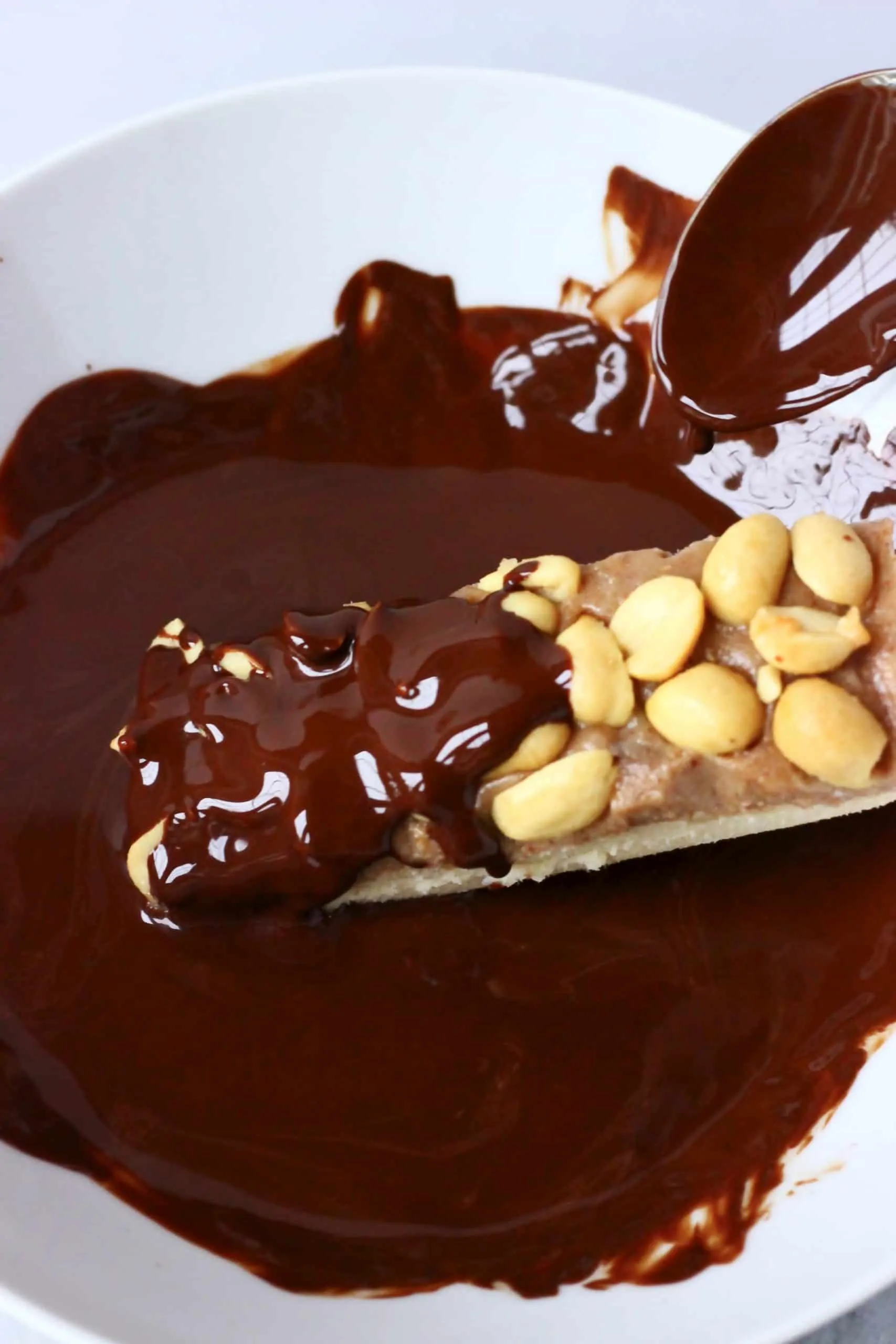A vegan snickers bar being dipped into a bowl of melted chocolate